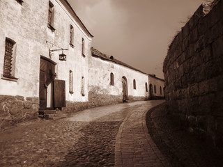 Old street with stone pavement and houses in courtyard of medieval castle. Photo in sepia