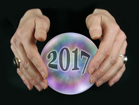 What will 2017 bring - Crystal Ball reading showing a 2017 inside a colorful translucent crystal ball between female hovering hands on a black background
