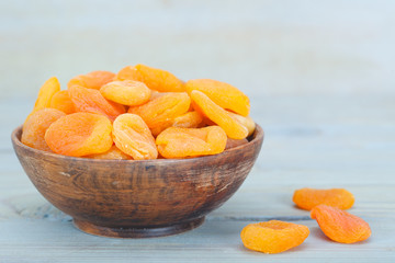 Delicious dried apricots in wooden bowl over blue background
