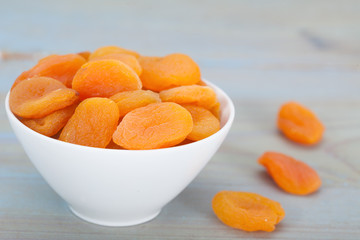 Healthy dried apricots in white bowl over blue background