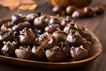Freshly roasted or baked chestnuts on wooden plate, photographed with natural light (Selective Focus, Focus one third into the image)