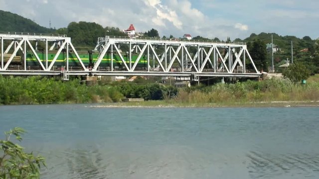 Товарный поезд, груженый песком, проходит по железнодорожному мосту через реку