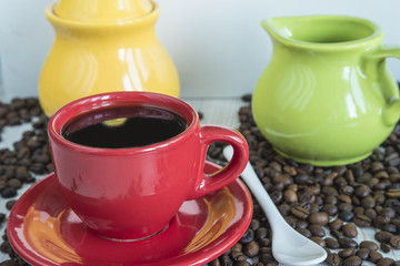 coffee concept: red cup of coffee, coffee beans, milk jug,sugar bowl on light background