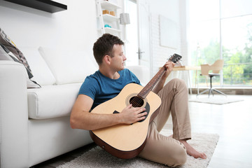 Young man playing guitar and sitting on the floor near the window