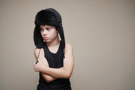 Boy in a cap with ear-flaps and a gymnastic undershirt on a light background. Conceptual image of the frozen person