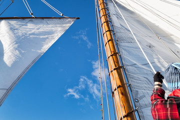 Sailboat crew raising white canvas sail. View looking up
