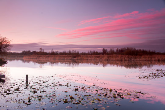 Roze zonsondergang boven de polder weerspiegelt in sloot