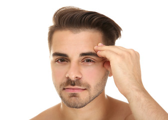 Young handsome man examining his face on white background
