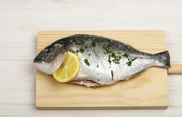 Close-up of a aw fish with lemon and green on a wooden board. Horizontal studio shot