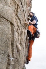 Handsome young man climbing natural rocky wall.