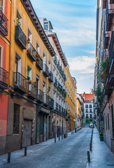 Quiet alley street scene, in Madrid, Spain.  Two women and a child at the far end, crossing the lane.  Colourful tall apartment buildings walls lined the street along with narrow sidewalks.