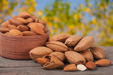 almonds in a bowl on the old wooden board with blurred garden background