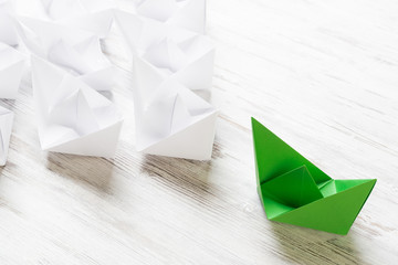 Business leadership concept with white and color paper boats on wooden table