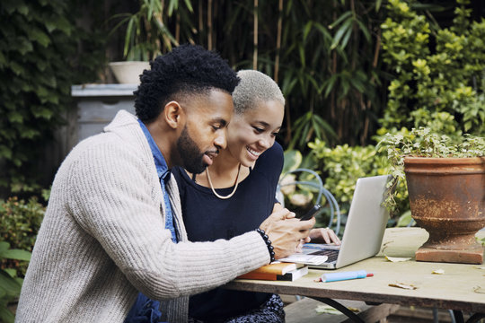 Happy couple using technology while sitting at table in the backyard