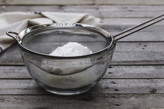 Close up of flour in sieve over bowl on wooden table