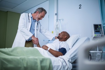 Happy doctor and patient shaking hand in ward - Powered by Adobe
