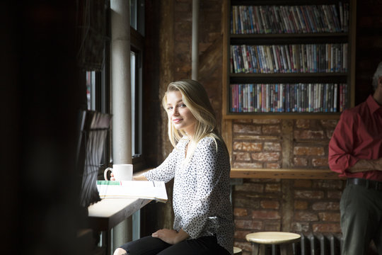 Portrait of smiling woman with newspaper having coffee at cafe