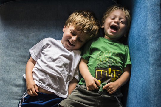 High angle view of happy brothers lying on sofa at home