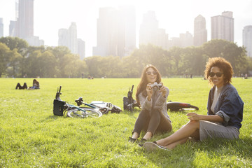 Happy woman holding camera while relaxing with friend on grassy field