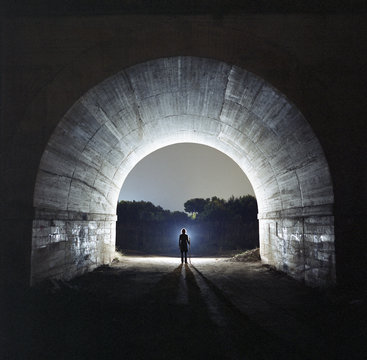 Silhouetted of man standing in tunnel at dusk
