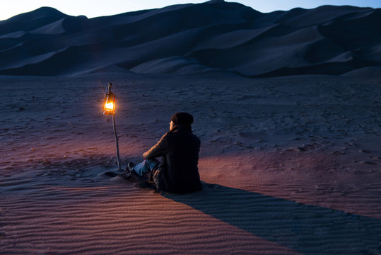 Rear view of man sitting on sand with illuminated lantern