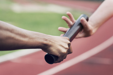 Cropped image of runner passing baton to teammate