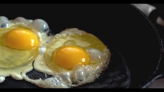 Two chicken eggs fried in a black frying pan on a gas stove.