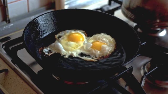 Two chicken eggs fried in a black frying pan on a gas stove.  Cooking omelette from two eggs.