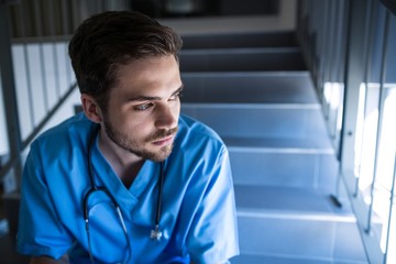 Thoughtful male nurse sitting on staircase