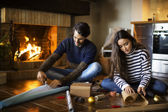 Couple wrapping gift boxes on floor by fireplace at home