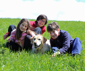 two boys and a girl with Labrador Retriever dog on the green gra