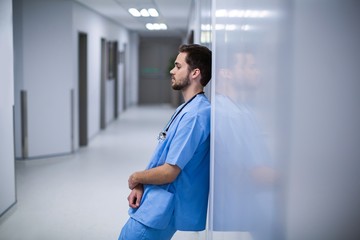 Tensed male nurse leaning on wall in corridor