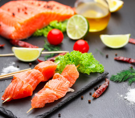 Raw salmon skewers on a stone plate. tomatoes, lime and lettuce for cooking.