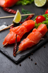 Raw salmon skewers on a stone plate. tomatoes, lime and lettuce for cooking.