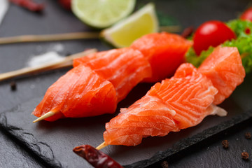 Raw salmon skewers on a stone plate. tomatoes, lime and lettuce for cooking.