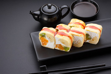 Sweet sushi roll in mamenori with kiwi, banana, orange and mascarpone on a stone plate.