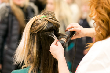 Fototapeta premium Close Up Rear View of Stylist Hairdresser Using Flat Iron on Hair Female Brunette Client.