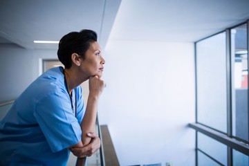 Thoughtful female nurse leaning on railing in corridor