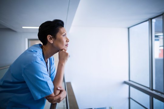 Thoughtful Female Nurse Leaning On Railing In Corridor