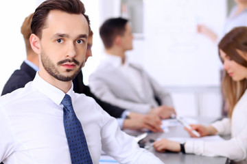 Portrait of cheerful smiling businessman  against a group of  people at meeting.