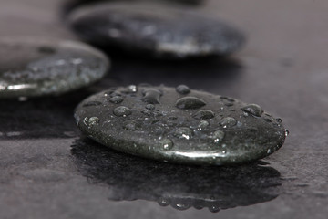 Spa background. Volcanic rocks on reflective background with raindrops. Relaxation, body care treatment, spa, wellness concept