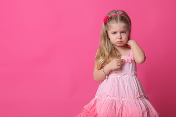 Sad baby in dress. Close up. Pink background