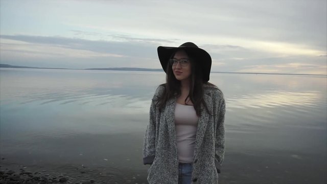 Young woman in black hat and glasses near the sea at sunset HD