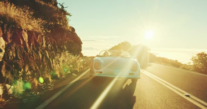 Happy couple driving on country road into the sunset in classic vintage sports car