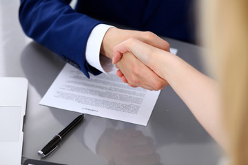 Businessman and business woman shaking hands to each other above signed contract