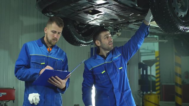 Young workshop employees working together underneath a lifted car