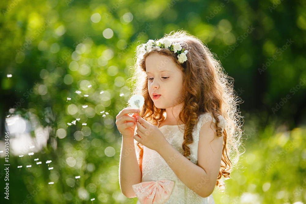 Wall mural Little curly girl blowing dandelion.