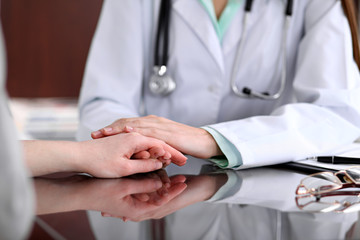 Friendly female doctor hands holding patient hand sitting at the desk for encouragement, empathy, cheering and support while medical examination. Bad news lessening, trust and medicine concept