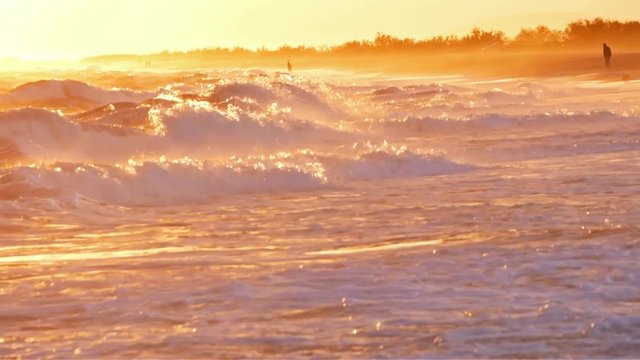 deux silhouettes au bord d'une plage avec les vagues d'une mer trés agitée au coucher de soleil 