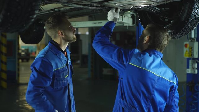 Young workshop employees working together underneath a lifted car